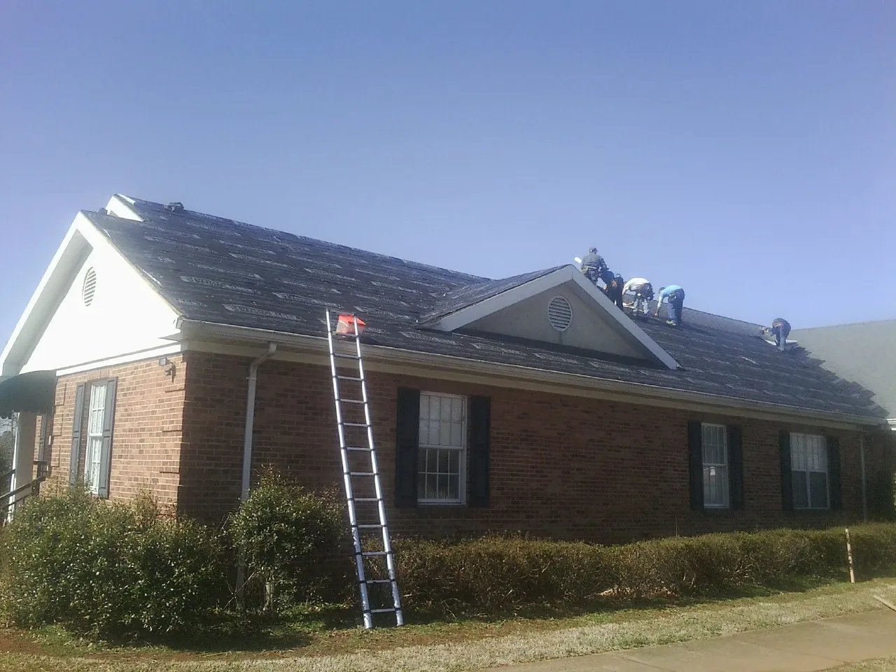 Crew tearing shingles off a brick ranch roof with a ladder set — Emergency Roof Repair work by our crew in Paul