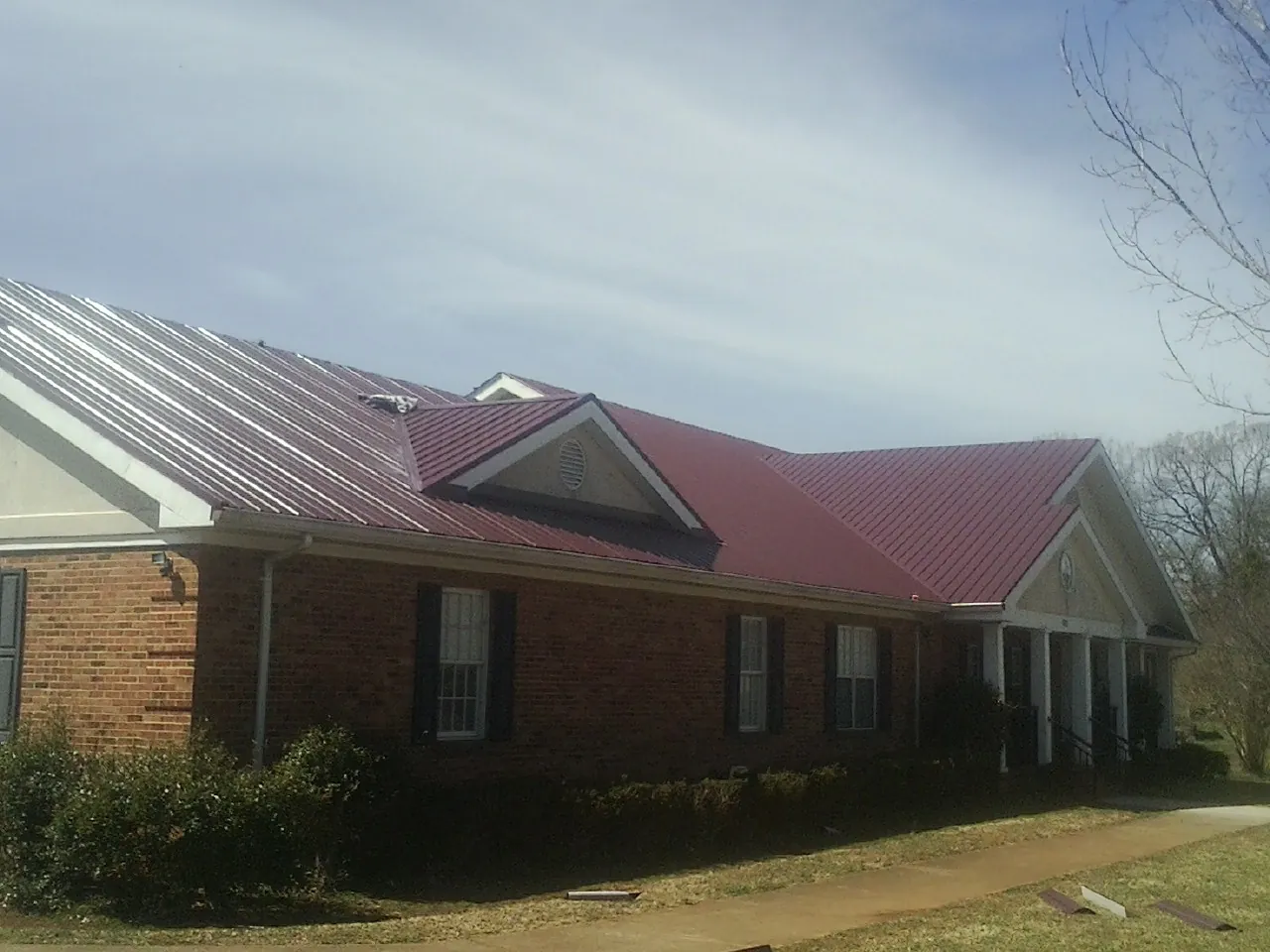 Red metal roof with gabled entries on a long brick building, from a Hail Damage Roof Repair job in Paul