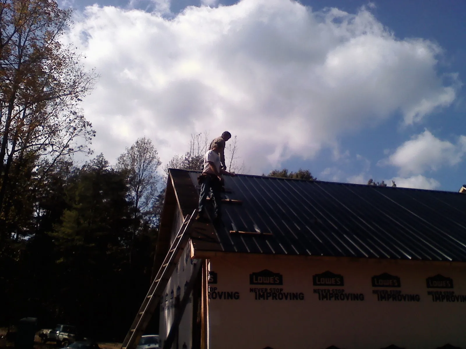 Roofer fastening dark metal panels high against a cloudy sky, from a Roof Inspection job in Paul