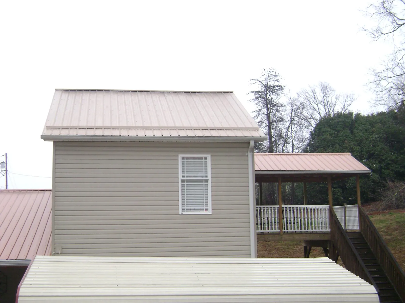 Tan metal roofs on a two story addition and attached porch, from a Roof Replacement job in Paul